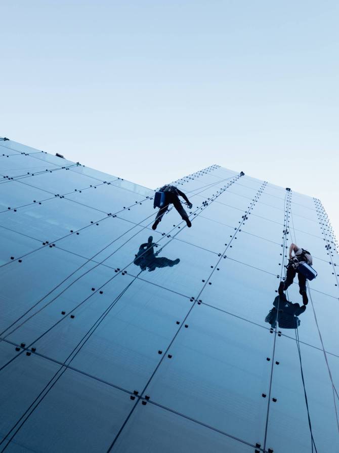A low angle shot of two persons rappelling at the side of a tall building